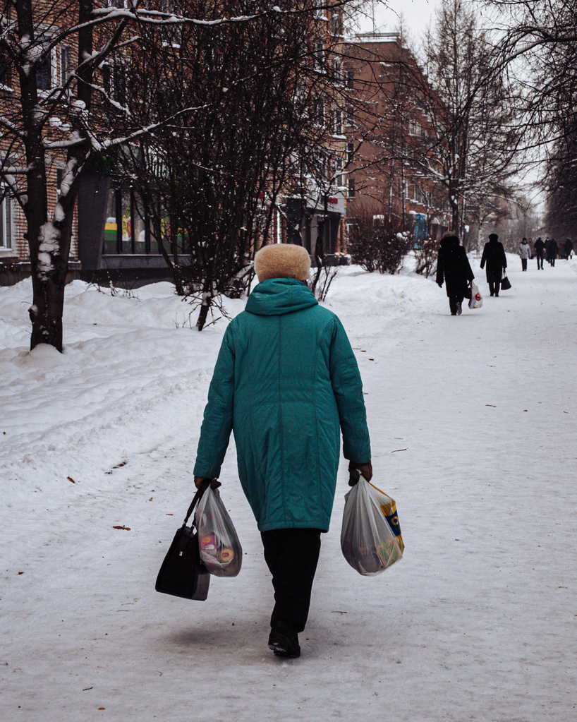 A Person Wearing Winter Clothing Walking on the Snow Covered Street while Carrying Grocery Bags