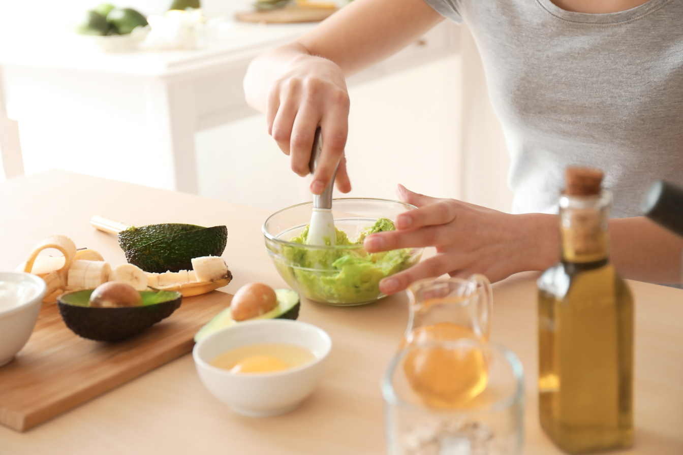 Woman Making Nourishing Mask with Avocado in Kitchen